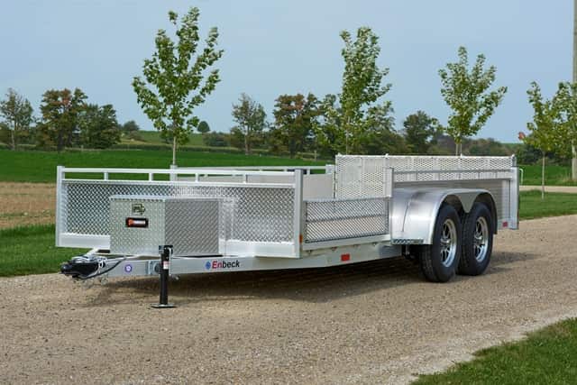 Silver Enbeck aluminum utility trailer with mesh sides on a gravel path in a grassy field.