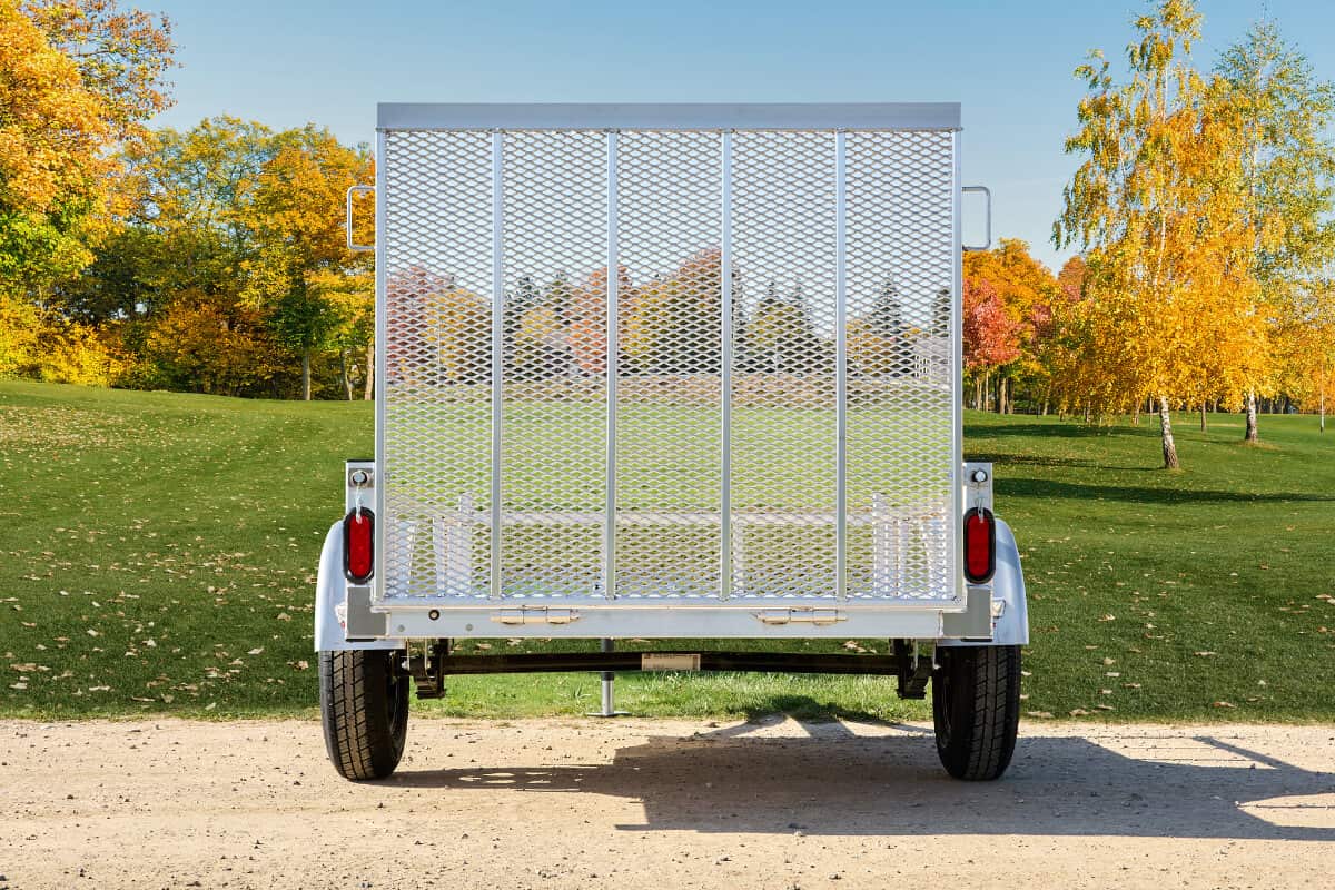 Rear view of a galvanized single-axle utility trailer with fold-down mesh tailgate, red tail lights, and tubular side rails.