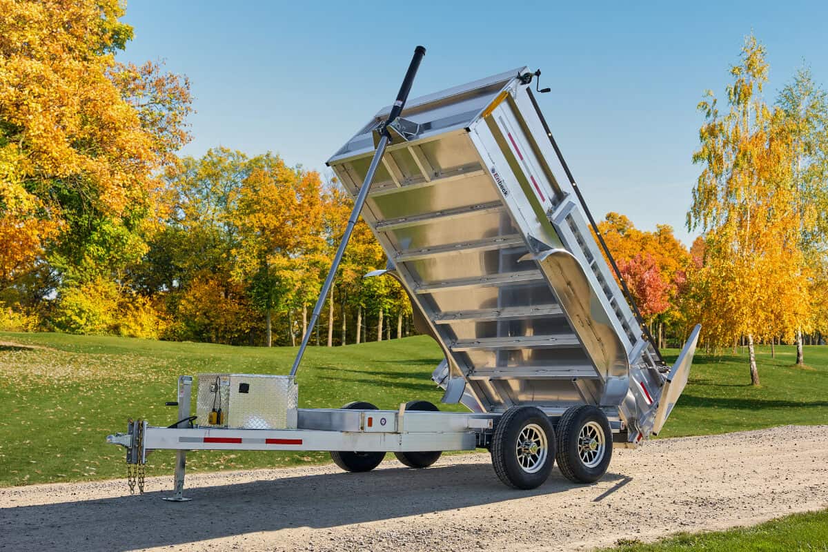 Angled front-side view of a tandem 5200 lbs dump trailer lifting its bed to full height, showing the open frame and dual-axle structure.